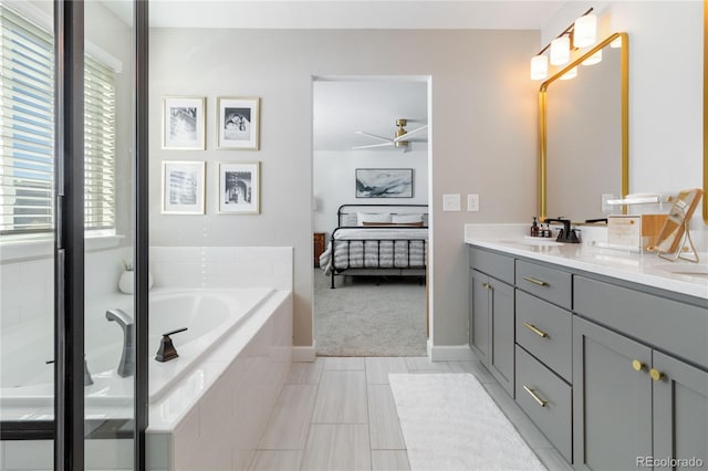 bathroom with ceiling fan, vanity, and tiled tub