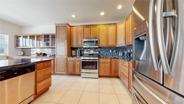 kitchen with light tile patterned floors, stainless steel appliances, dark stone counters, and backsplash