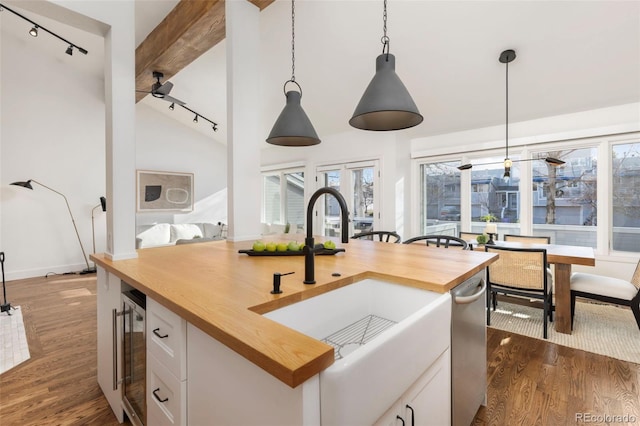 kitchen with butcher block counters, sink, white cabinetry, lofted ceiling with beams, and hanging light fixtures