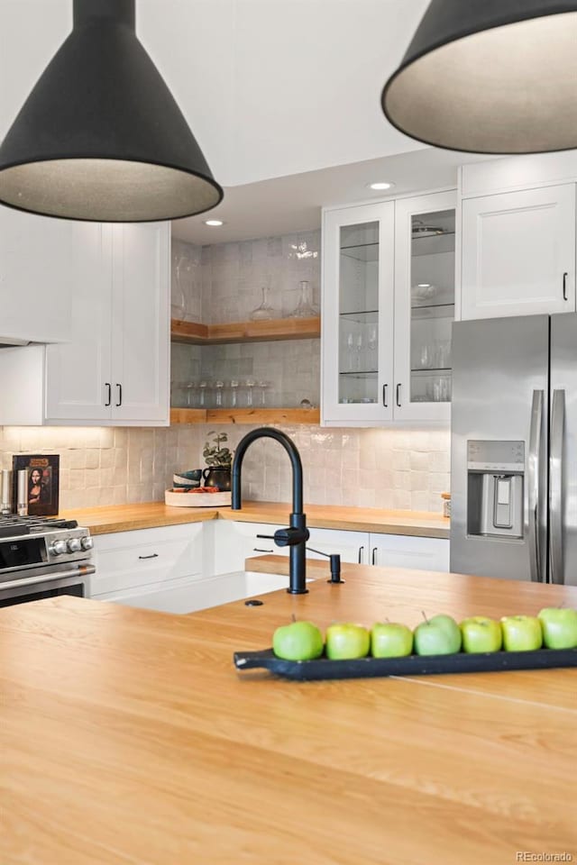 kitchen with backsplash, stainless steel appliances, wooden counters, and white cabinets