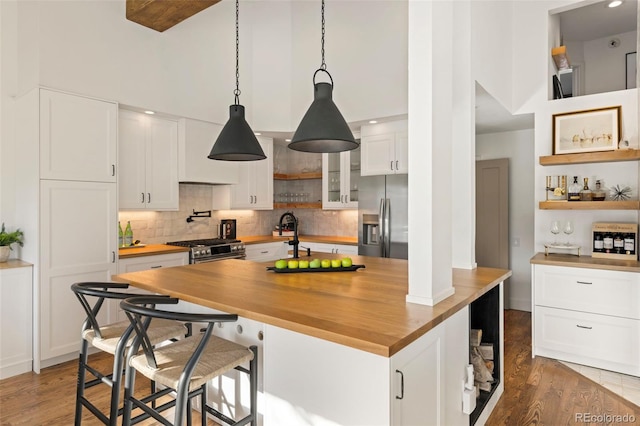 kitchen with stainless steel appliances, white cabinets, wooden counters, and decorative light fixtures