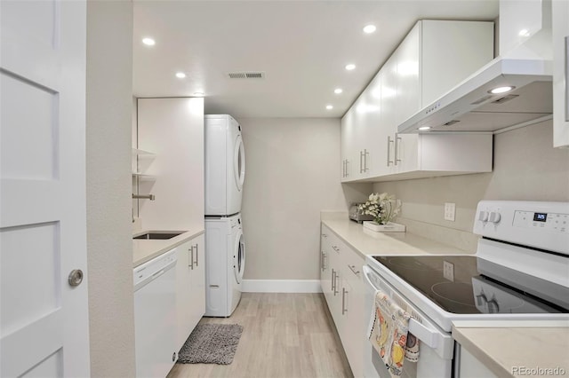 kitchen with stacked washer / drying machine, wall chimney range hood, white appliances, and white cabinetry