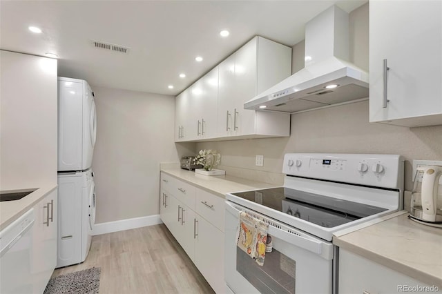 kitchen with stacked washer and clothes dryer, white appliances, light wood-type flooring, wall chimney range hood, and white cabinets