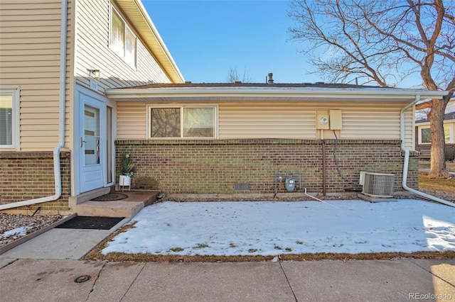 snow covered rear of property featuring central AC unit