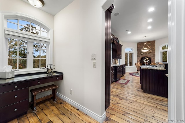 kitchen with light wood-type flooring, a fireplace, built in desk, hanging light fixtures, and dark brown cabinetry