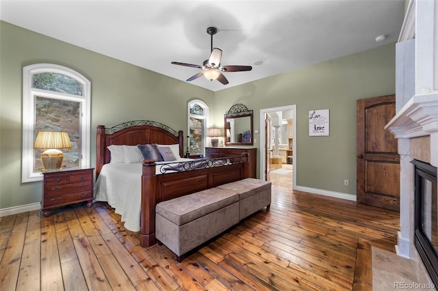 bedroom with connected bathroom, wood-type flooring, a tile fireplace, and ceiling fan