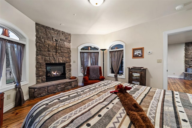 bedroom with hardwood / wood-style floors and a stone fireplace