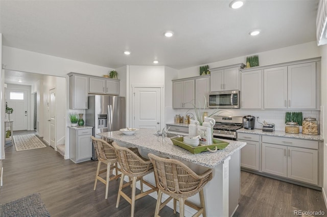 kitchen featuring a kitchen breakfast bar, gray cabinetry, a kitchen island with sink, and appliances with stainless steel finishes