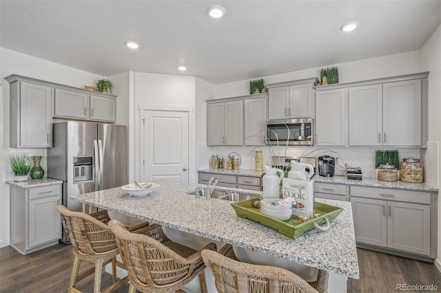 kitchen with a kitchen breakfast bar, gray cabinetry, stainless steel appliances, sink, and an island with sink