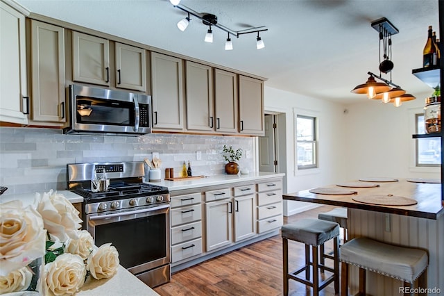 kitchen with decorative backsplash, appliances with stainless steel finishes, hanging light fixtures, and light wood-type flooring