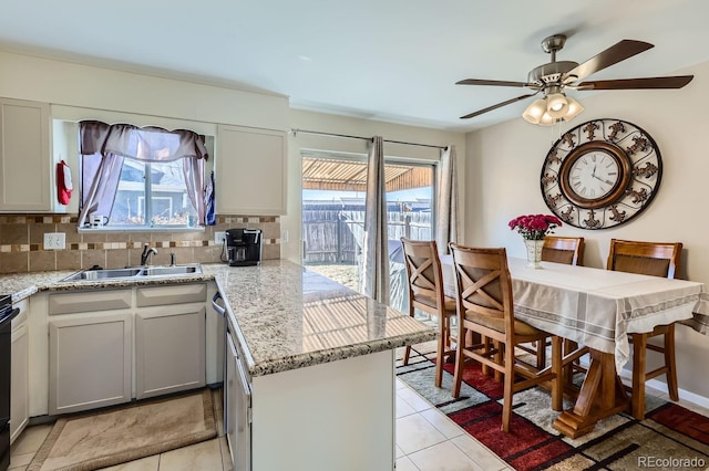 kitchen featuring sink, light stone counters, light tile patterned flooring, decorative backsplash, and kitchen peninsula