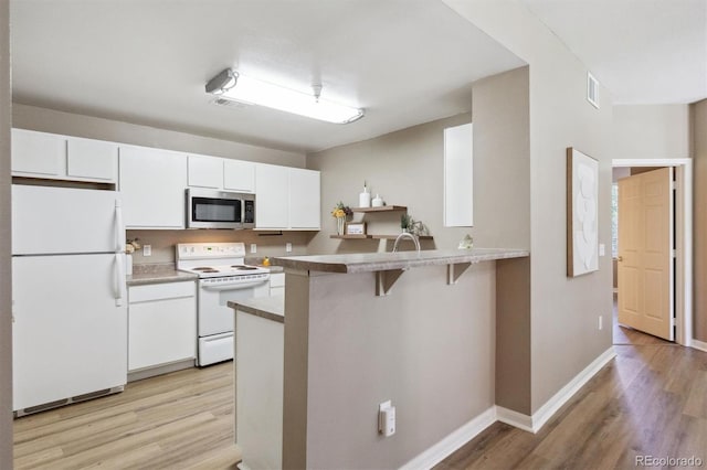 12914 Ironstone Way Unit 102, Parker, CO 80134 - kitchen featuring white appliances, light wood finished floors, white cabinets, a kitchen breakfast bar, and baseboards