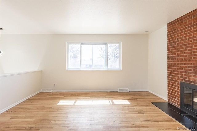 unfurnished living room with visible vents, baseboards, light wood-style floors, and a brick fireplace