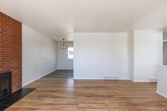 unfurnished living room with visible vents, a brick fireplace, light wood-type flooring, and baseboards