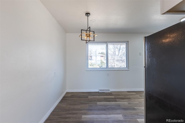 unfurnished dining area featuring dark wood finished floors, an inviting chandelier, baseboards, and visible vents