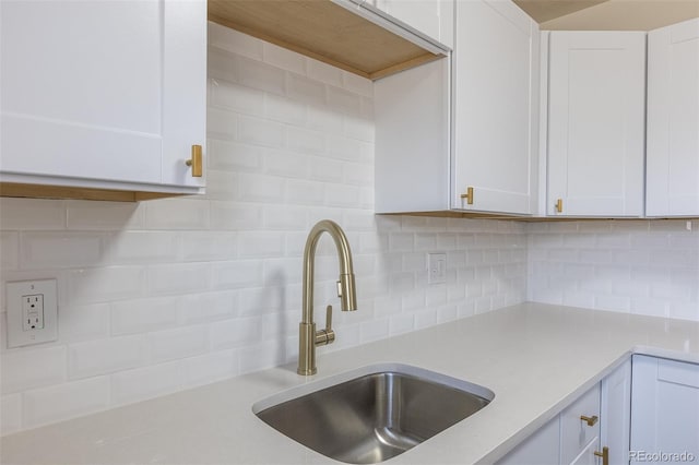 kitchen featuring a sink, backsplash, light countertops, and white cabinetry