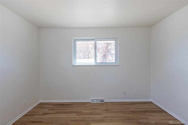 unfurnished room featuring wood finished floors, visible vents, and baseboards