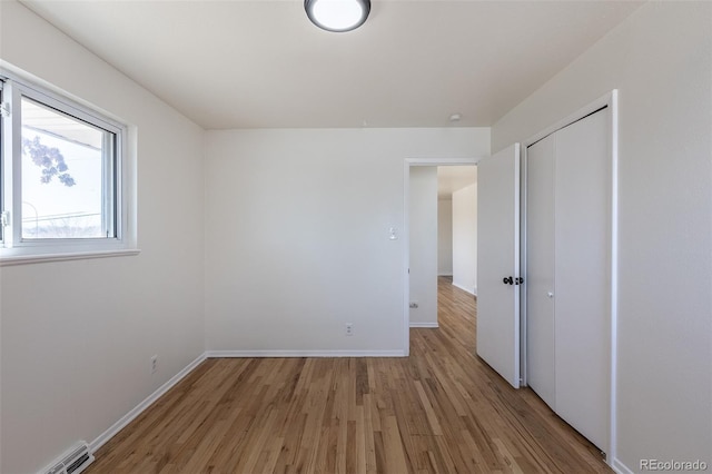 unfurnished bedroom with a closet, baseboards, visible vents, and light wood finished floors