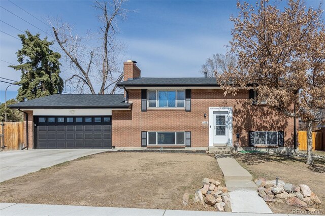 bi-level home featuring an attached garage, a chimney, driveway, and fence