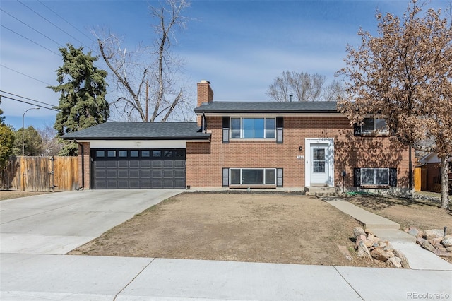 split foyer home with fence, concrete driveway, an attached garage, brick siding, and a chimney