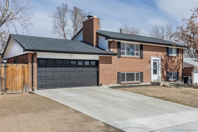 split foyer home featuring a garage, brick siding, driveway, and fence