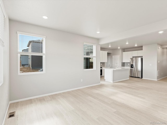 unfurnished living room with sink, a wealth of natural light, and light wood-type flooring