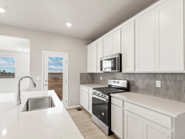 kitchen with light stone counters, sink, white cabinets, and appliances with stainless steel finishes