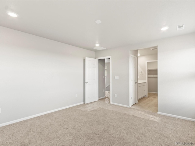 unfurnished bedroom with ensuite bathroom, light colored carpet, a closet, and a spacious closet