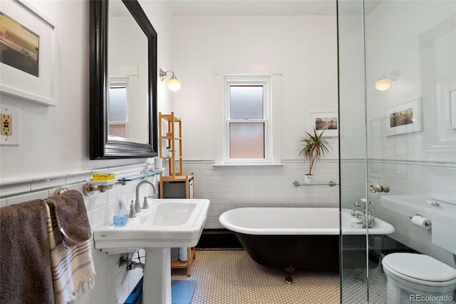 328 S Lincoln St, Denver, CO 80209 - bathroom with tile walls, wainscoting, a freestanding bath, tile patterned flooring, and toilet