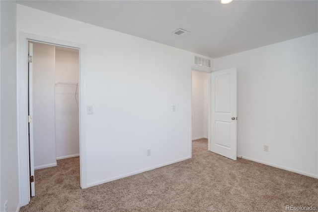 unfurnished bedroom with light colored carpet, a walk in closet, and a closet