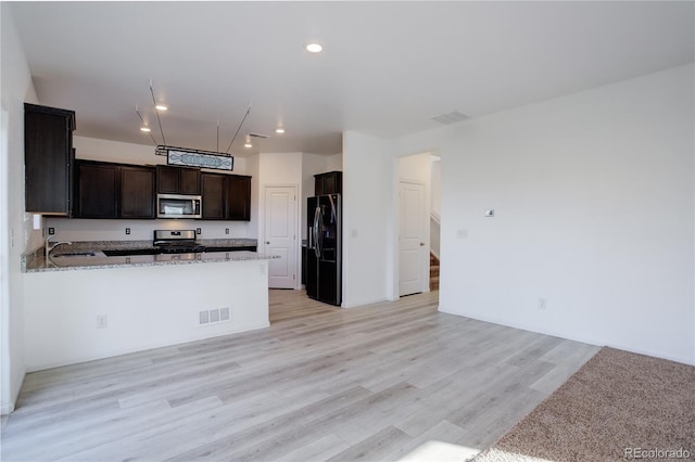 kitchen with light wood-type flooring, kitchen peninsula, light stone counters, and appliances with stainless steel finishes