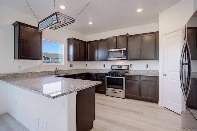 kitchen with kitchen peninsula, appliances with stainless steel finishes, light stone countertops, sink, and decorative light fixtures