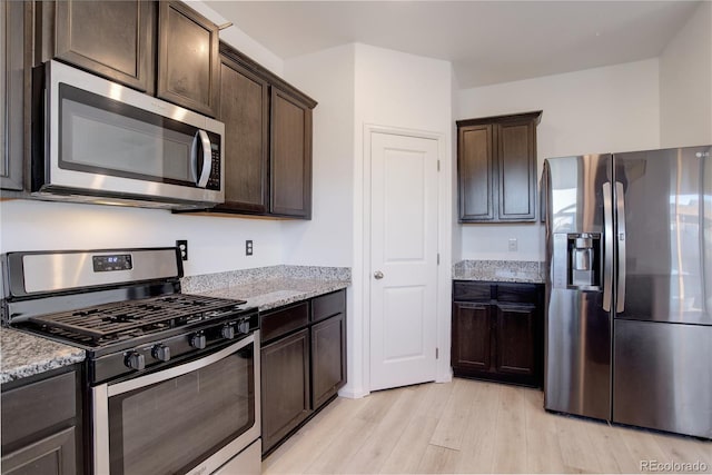 kitchen featuring dark brown cabinetry, light stone counters, stainless steel appliances, and light wood-type flooring