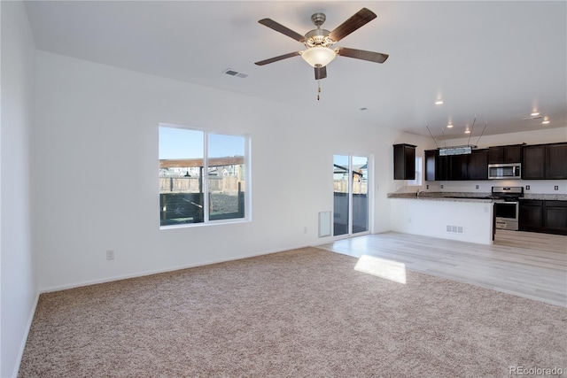 unfurnished living room featuring ceiling fan, sink, and light colored carpet