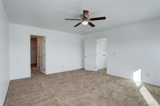 unfurnished bedroom with a spacious closet, a closet, ceiling fan, and light carpet