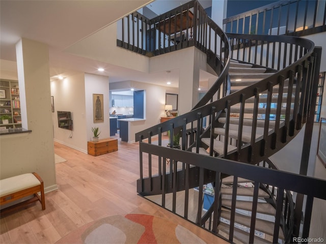 stairway featuring a high ceiling, baseboards, and wood finished floors