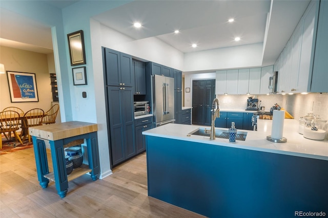 kitchen with a peninsula, stainless steel appliances, light countertops, light wood-type flooring, and a sink