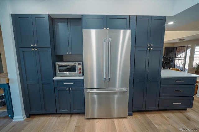 kitchen featuring light wood finished floors, a toaster, high end refrigerator, light countertops, and blue cabinetry