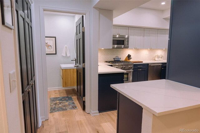 kitchen featuring light wood finished floors, decorative backsplash, appliances with stainless steel finishes, light stone countertops, and white cabinetry