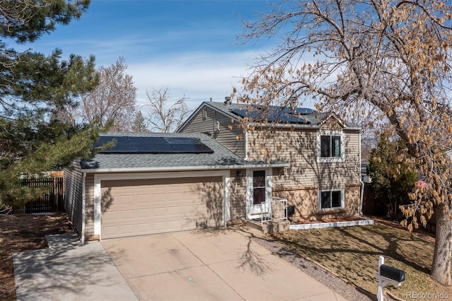 split level home featuring driveway, roof mounted solar panels, fence, roof with shingles, and a garage