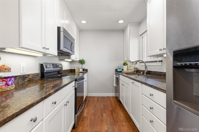 kitchen featuring dark wood finished floors, dark stone counters, a sink, white cabinets, and appliances with stainless steel finishes