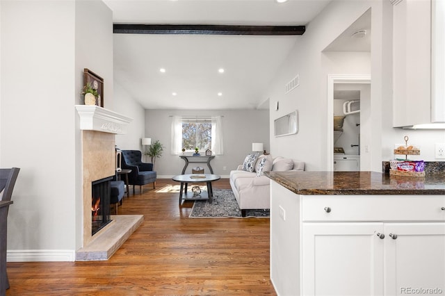 living area with visible vents, vaulted ceiling with beams, baseboards, a premium fireplace, and light wood-style flooring