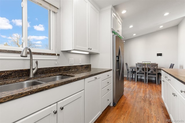 kitchen featuring stainless steel fridge, white cabinetry, light wood-style floors, and a sink