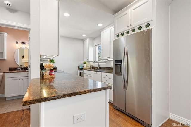 kitchen with a peninsula, stainless steel fridge with ice dispenser, a sink, white cabinetry, and light wood-type flooring