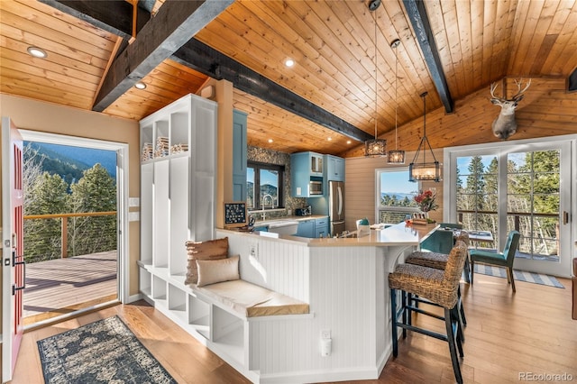 kitchen with freestanding refrigerator, blue cabinetry, wooden ceiling, light countertops, and a breakfast bar area