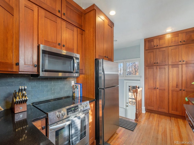 kitchen with appliances with stainless steel finishes, decorative backsplash, light hardwood / wood-style floors, and dark stone counters