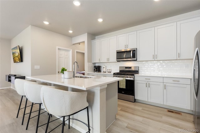 6150 Sugarloaf St, Brighton, CO 80601 - kitchen featuring appliances with stainless steel finishes, light wood-style flooring, backsplash, a center island with sink, and light countertops