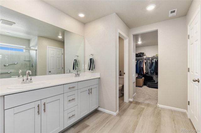 6150 Sugarloaf St, Brighton, CO 80601 - bathroom featuring wood finished floors, double vanity, a shower stall, a spacious closet, and recessed lighting