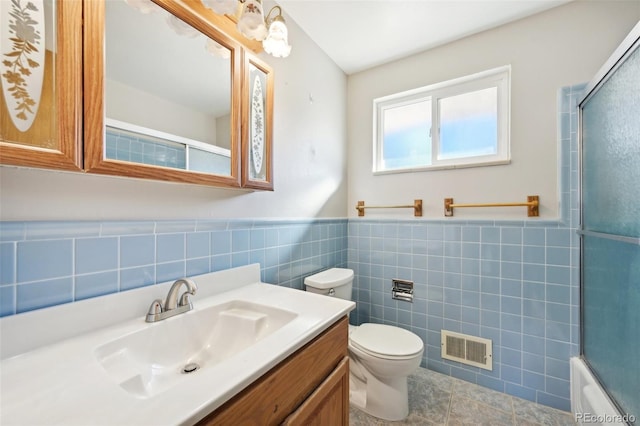 full bathroom featuring toilet, tile walls, bath / shower combo with glass door, tile patterned flooring, and vanity