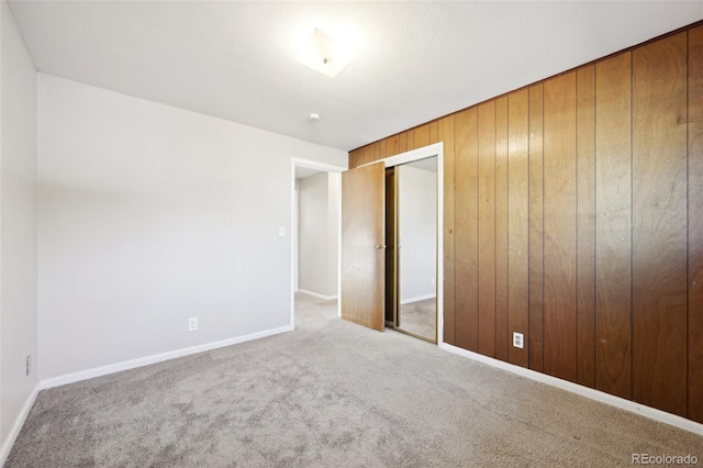 unfurnished bedroom featuring light colored carpet, wooden walls, and a closet